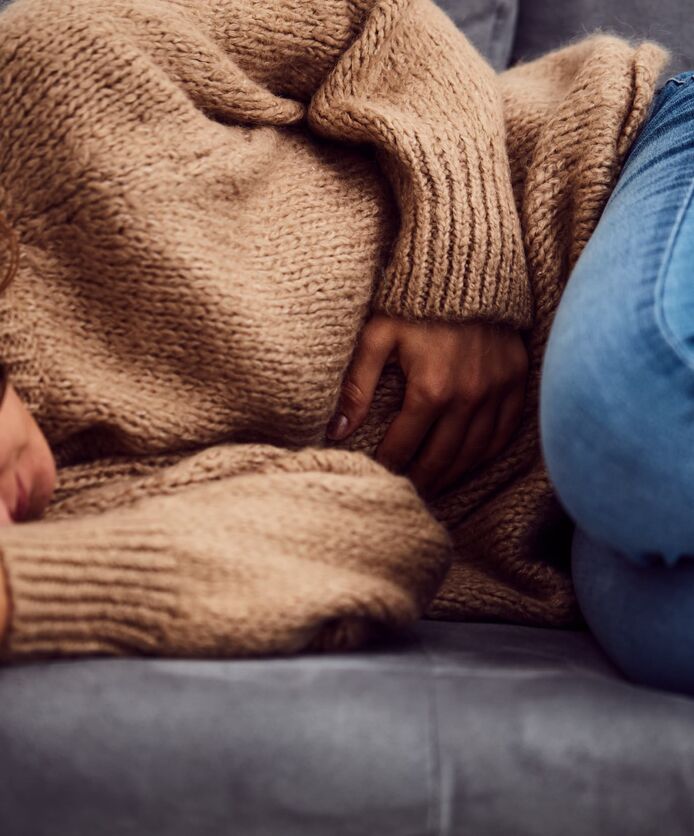 A woman lies down, holding her abdomen in pain