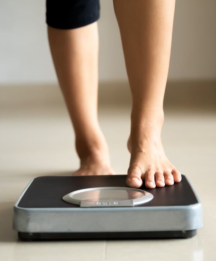 A woman wearing ¾ length leggings steps barefoot onto a set of digital scales.
