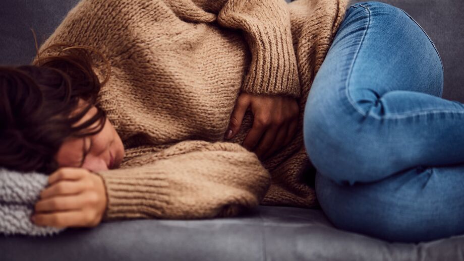 A woman lies down, holding her abdomen in pain