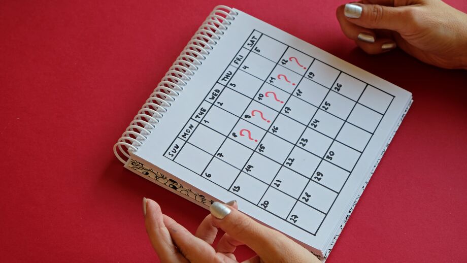 A woman crosses her fingers while looking at a calendar where five days are marked with a red question mark